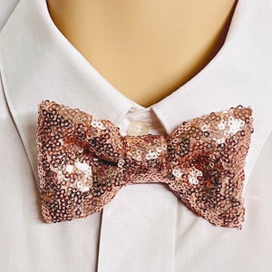May include: A rose gold sequined bow tie. The bow tie is made of small, shimmering sequins and is a festive accessory for any occasion.