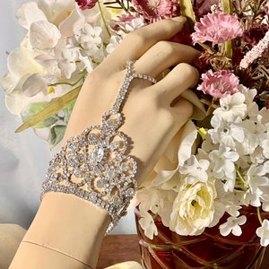 May include: A silver rhinestone bracelet with a delicate floral design. The bracelet features a large, clear rhinestone in the center and is accented with smaller rhinestones.