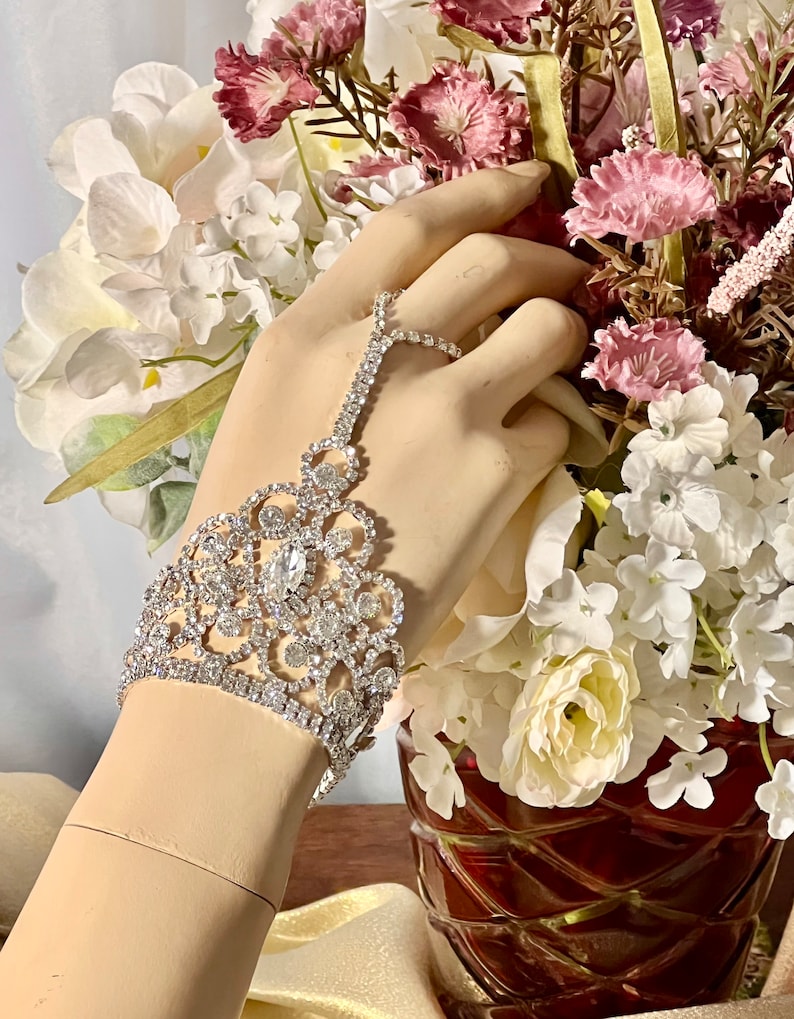 May include: A silver rhinestone bracelet with a delicate floral design. The bracelet features a large, clear rhinestone in the center and is accented with smaller rhinestones.