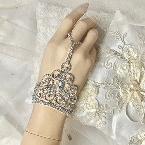 May include: A silver rhinestone bracelet with a delicate floral design. The bracelet has a finger loop and is perfect for a wedding or special occasion.