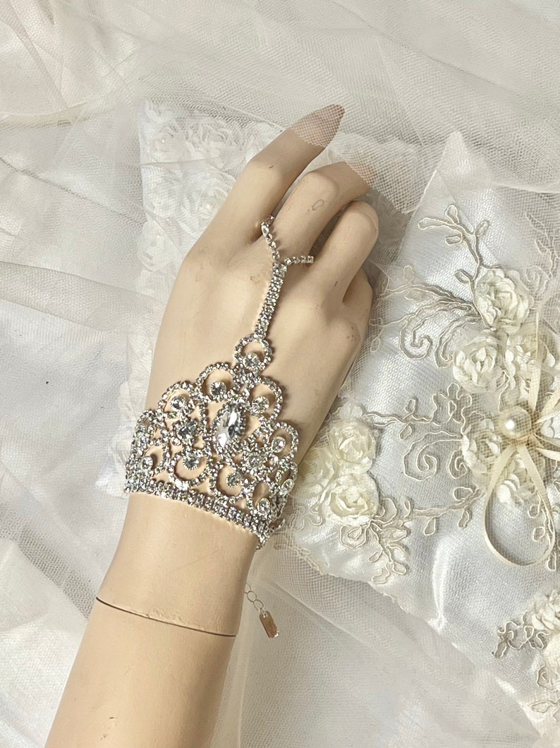 May include: A silver rhinestone bracelet with a delicate floral design. The bracelet has a finger loop and is perfect for a wedding or special occasion.