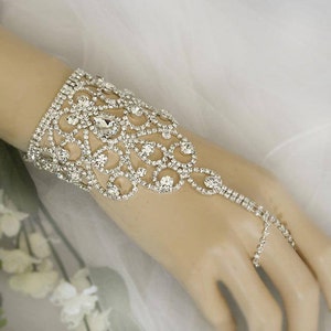 May include: A silver rhinestone bracelet with a delicate, intricate design. The bracelet features a chain that extends to the finger, creating a unique and elegant look.