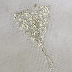 May include: A silver ankle bracelet with a delicate, intricate design featuring a large cluster of clear rhinestones.