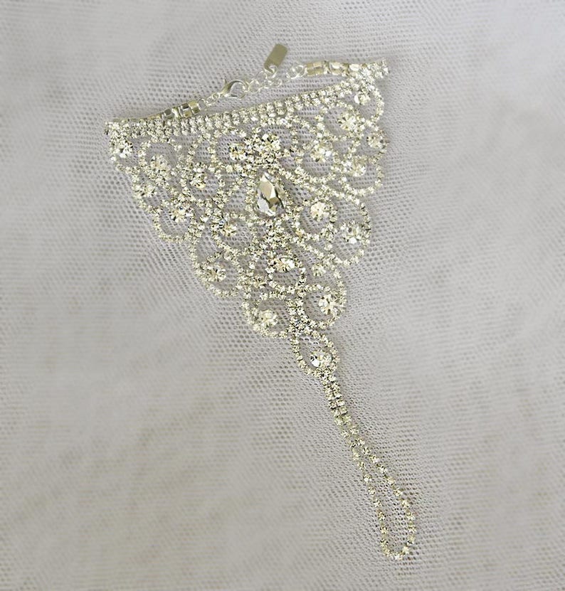 May include: A silver ankle bracelet with a delicate, intricate design featuring a large cluster of clear rhinestones.
