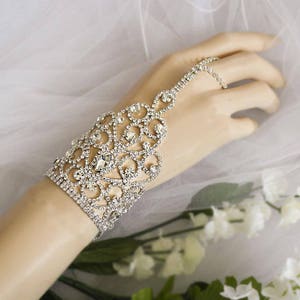 May include: A silver rhinestone bracelet with a delicate, intricate design. The bracelet is adorned with sparkling rhinestones and features a finger loop.