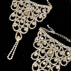May include: A pair of silver ankle bracelets with a delicate, intricate design. Each bracelet is adorned with sparkling rhinestones, creating a glamorous and elegant look.