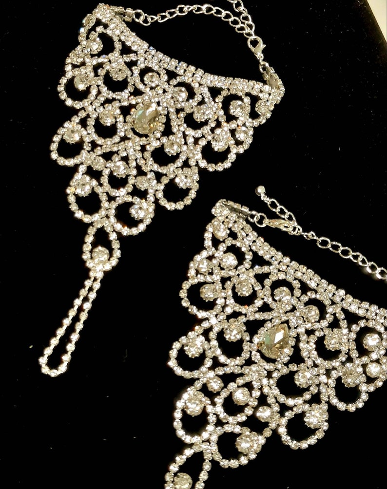 May include: A pair of silver ankle bracelets with a delicate, intricate design. Each bracelet is adorned with sparkling rhinestones, creating a glamorous and elegant look.
