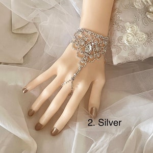 May include: A silver rhinestone bracelet with a finger ring attachment. The bracelet has a floral design and is adorned with sparkling rhinestones.