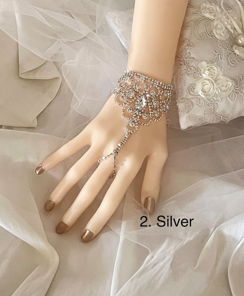 May include: A silver rhinestone bracelet with a finger ring attachment. The bracelet has a floral design and is adorned with sparkling rhinestones.