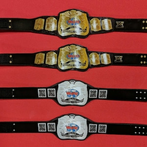 May include: Four wrestling championship belts. Two belts have gold and black designs with the text "World Tag Team Wrestling Champions". The other two belts have silver and black designs with the text "World Tag Team Wrestling Champions".