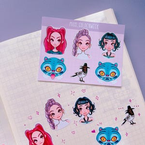 Könnte beinhalten: Ein Stickerbogen mit der Aufschrift MISS_GOLDENWEEK zeigt Illustrationen von drei Charakteren mit verschiedenen Frisuren, zwei blauen tigerartigen Wesen mit gelben Augen und einem Vogel mit Hut. Einzelne Sticker kleben auf dem karierten Papier.
