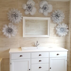 Puede incluir: Mueble de ba&ntilde;o blanco con un lavabo de porcelana blanca y un grifo cromado. El mueble tiene seis cajones y dos puertas. La pared detr&aacute;s del mueble est&aacute; alicatada en un color beige claro y decorada con seis grandes flores de papel grises.