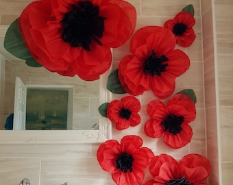 May include: A set of red paper flowers with black centers, arranged on a tiled wall. The flowers are various sizes and are a popular decoration for events.