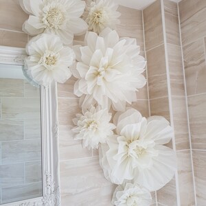 Puede incluir: Un ba&ntilde;o con azulejos blancos decorado con grandes flores de papel blanco. Las flores est&aacute;n dispuestas en un racimo en la pared, creando un ambiente caprichoso y elegante.