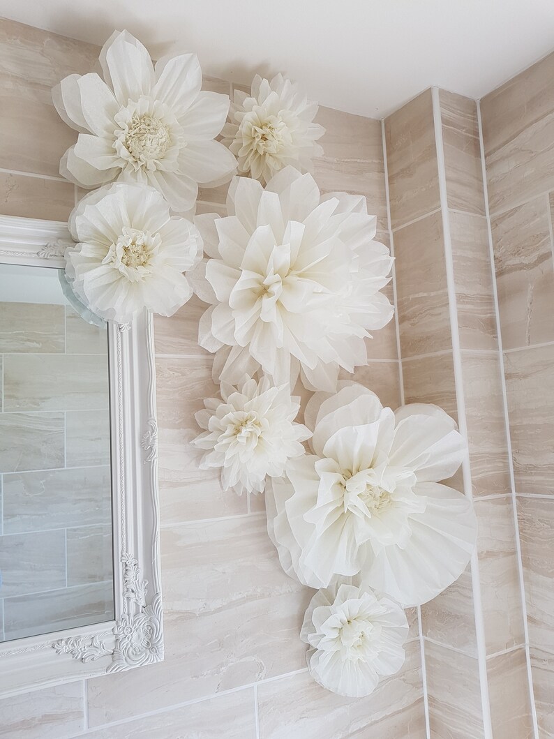 Puede incluir: Un ba&ntilde;o con azulejos blancos decorado con grandes flores de papel blanco. Las flores est&aacute;n dispuestas en un racimo en la pared, creando un ambiente caprichoso y elegante.