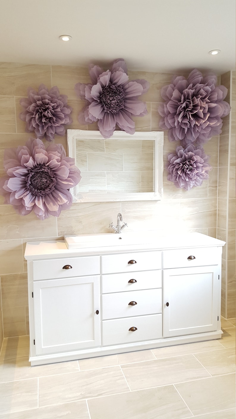 Puede incluir: Mueble de ba&ntilde;o blanco con cuatro cajones y una puerta de armario. El mueble tiene una encimera blanca y un grifo cromado. La pared detr&aacute;s del mueble est&aacute; alicatada y decorada con grandes flores de papel morado.