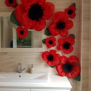 May include: A bathroom decorated with red paper flowers. The flowers are arranged on the wall in a cluster, with the largest flower at the top. The flowers are made of tissue paper and have a black center. The bathroom has a white sink and vanity.