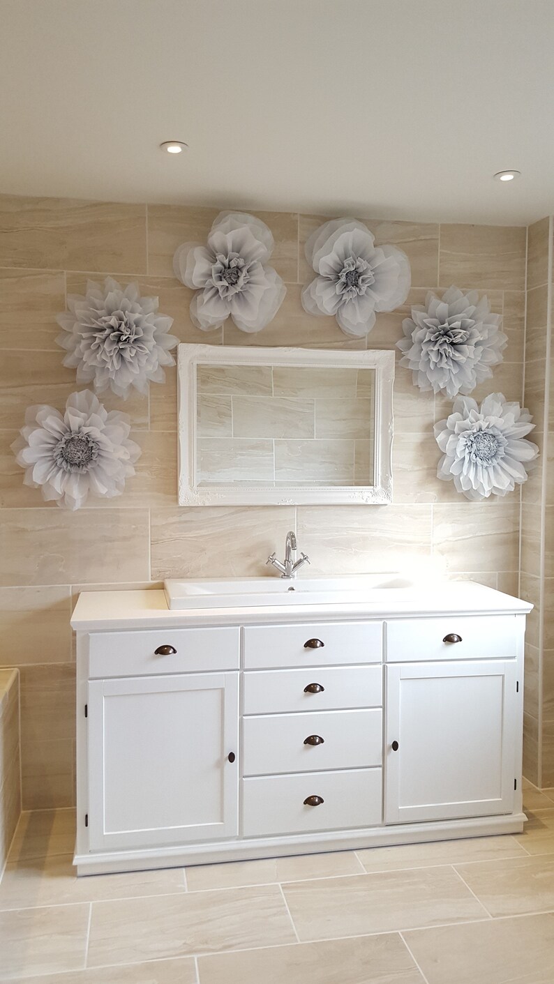 May include: White bathroom vanity with a white porcelain sink and chrome faucet. The vanity has five drawers and two doors. The wall behind the vanity is tiled and decorated with gray paper flowers.