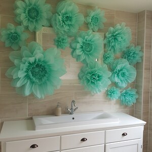 May include: A white bathroom vanity with a white porcelain sink and a chrome faucet. The wall behind the vanity is decorated with large, light green paper flowers.