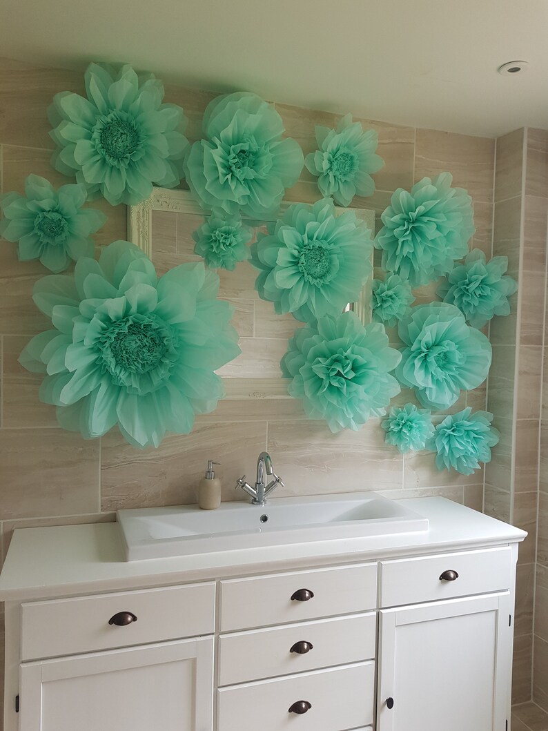 May include: A white bathroom vanity with a white porcelain sink and a chrome faucet. The wall behind the vanity is decorated with large, light green paper flowers.