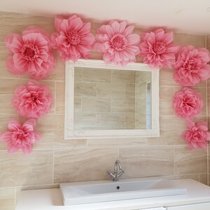Puede incluir: Un ba&ntilde;o decorado con grandes flores de papel rosa, un espejo blanco enmarcado y un lavabo de porcelana blanca.