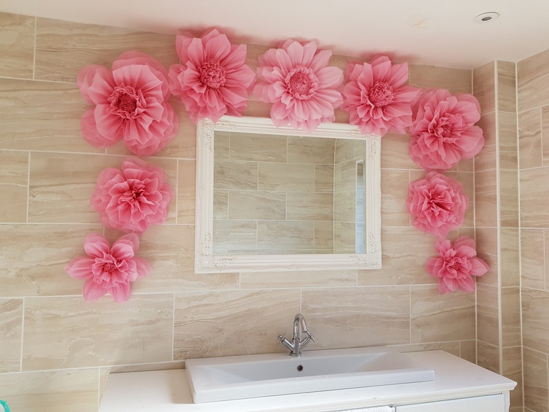 Puede incluir: Un ba&ntilde;o decorado con grandes flores de papel rosa, un espejo blanco enmarcado y un lavabo de porcelana blanca.