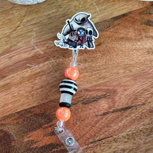May include: A black and white striped bead charm with orange beads and a clear plastic badge holder. The charm features a cartoon image of Jack Skellington, Sally, and Zero from the Nightmare Before Christmas.