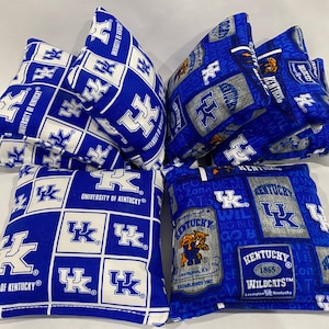 May include: A set of eight blue and white bean bags with the University of Kentucky logo and Wildcats text. The bean bags are made of fabric and have a variety of designs.