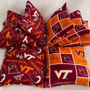May include: Set of six bean bags featuring a Virginia Tech Hokies theme. The bean bags are made of maroon and orange fabric with a white VT logo and a cartoon Hokie bird. The bean bags are perfect for playing cornhole or other games.