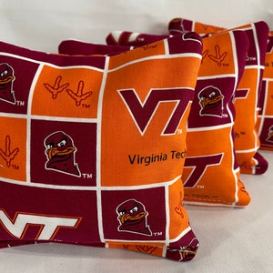 May include: Set of six bean bags featuring a maroon and orange checkered pattern with the Virginia Tech logo, a mascot, and the words "Virginia Tech" and "TM".