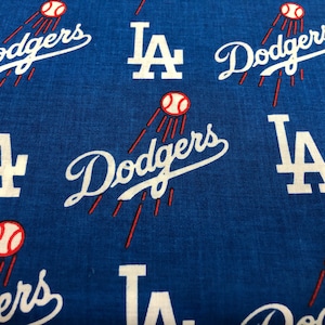 May include: Blue fabric with a repeating pattern of the Los Angeles Dodgers logo, including the team name in white script and the letters "LA" in white. Baseball graphics with red streaks are also present.