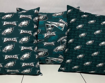 May include: Three green and white throw pillows featuring the Philadelphia Eagles logo and team name. The pillows are made from fabric and have a soft, comfortable feel.