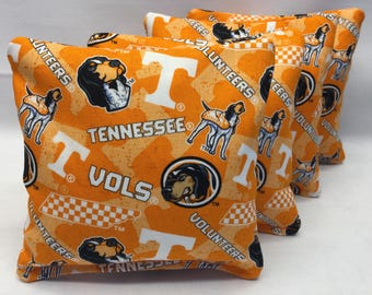 May include: Four orange bean bags with a white checkerboard pattern, a white "T" and the words "Tennessee Vols" and "Volunteers". The bean bags also feature a black and white illustration of a hound dog.