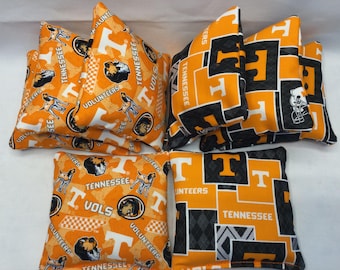 May include: Set of eight orange and black bean bags with the University of Tennessee Volunteers logo and various designs. The bags are made of fabric and have a checkered pattern.