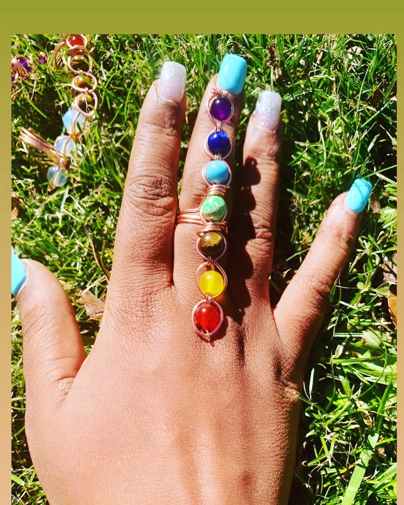 May include: A copper wire ring with seven colorful gemstones, representing the seven chakras, worn on a finger.