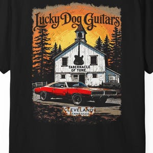 Może przedstawiać: Czarna koszulka z grafiką przedstawiającą biały kościół, czerwony samochód i napis "Lucky Dog Guitars". Projekt zawiera słowa "Tabernacle of Tone" i "Cleveland, Tennessee".