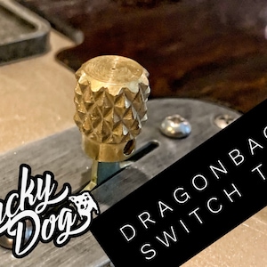 Puede incluir: Primer plano de una perilla de interruptor de color dorado con un patr&oacute;n de diamante. El interruptor est&aacute; etiquetado como "Dragonback Switch Tips" en texto negro sobre fondo blanco.