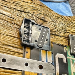 Op de afbeelding: Close-up van een gitaarbrug met een zwarte pickup en een metalen plaat met zes schroeven. De brug is gemaakt van metaal en heeft een zilveren afwerking. De gitaarbody is gemaakt van hout en heeft een natuurlijke afwerking.