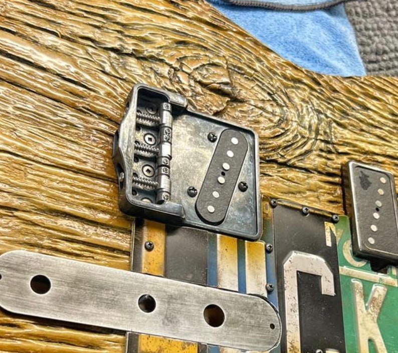 Op de afbeelding: Close-up van een gitaarbrug met een zwarte pickup en een metalen plaat met zes schroeven. De brug is gemaakt van metaal en heeft een zilveren afwerking. De gitaarbody is gemaakt van hout en heeft een natuurlijke afwerking.