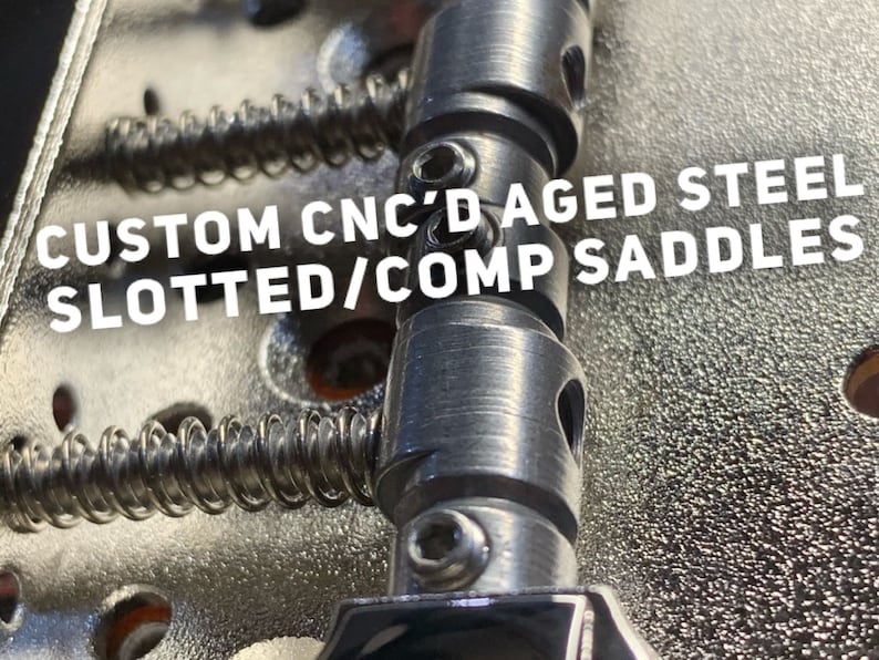 Op de afbeelding: Close-up van een gitaarbrug met aangepaste CNC-gefreesde, verouderde stalen gesleufde/comp-zadels. De zadels zijn zilverkleurig en hebben een textuur.