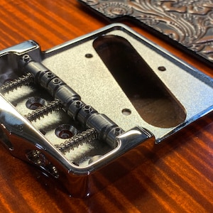 Op de afbeelding: Een chromen gitaarbrug met drie verstelbare zadels en een verchroomde basisplaat.