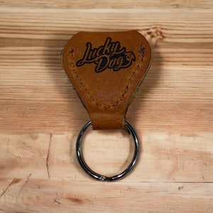 May include: A brown leather key chain with a silver ring. The leather has the words "Lucky Dog" embossed on it.