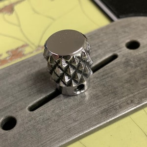 Puede incluir: Un pomo de color plateado en forma de diamante con una parte superior lisa y reflectante. El pomo est&aacute; montado en una superficie met&aacute;lica.