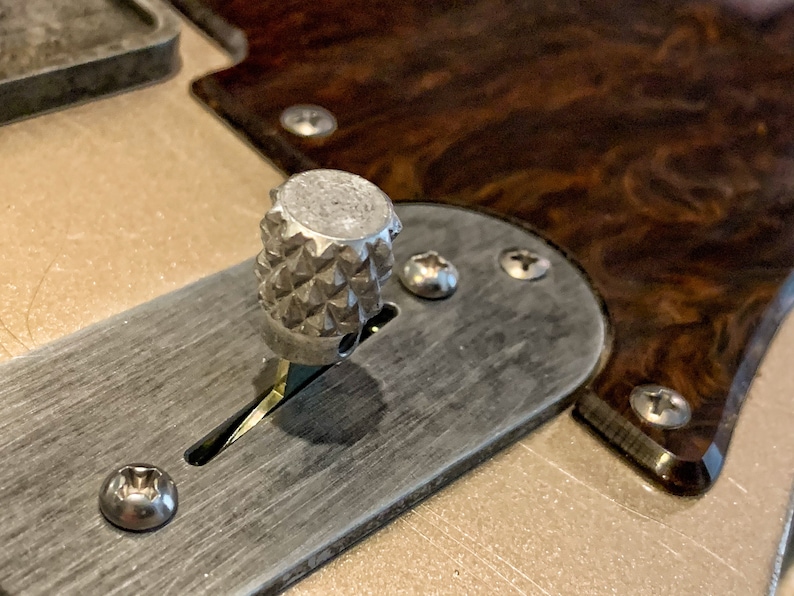 Puede incluir: Primer plano de una perilla de guitarra plateada con un patr&oacute;n texturizado en forma de diamante. La perilla est&aacute; unida a una placa plateada con tornillos.
