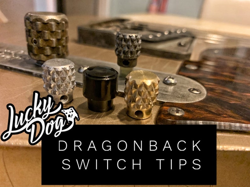 Puede incluir: Cuatro puntas de interruptor diferentes para una guitarra. Las puntas est&aacute;n hechas de metal y tienen un patr&oacute;n texturizado en forma de diamante. Las puntas son de varios colores, incluyendo plata, negro y oro. El texto "Lucky Dog" y "Dragonback Switch Tips" es visible en la imagen.