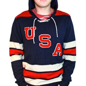 May include: A navy blue hooded sweater with white and red stripes. The sweater has a lace-up neckline and a large red felt "USA" graphic on the front.
