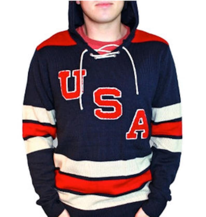 May include: A navy blue hooded sweater with white and red stripes. The sweater has a lace-up neckline and a large red felt "USA" graphic on the front.