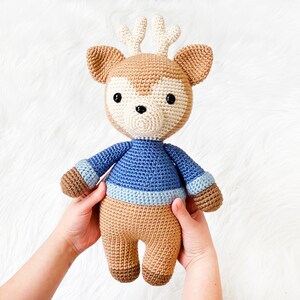 May include: A crocheted deer toy wearing a blue and white striped sweater. The deer has brown fur, white antlers, and black eyes.