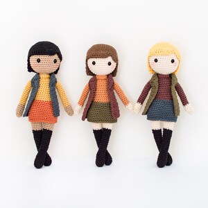 May include: Three crocheted dolls wearing different colored outfits. The dolls have brown hair, black hair, and blonde hair. They are all wearing skirts, vests, and boots.
