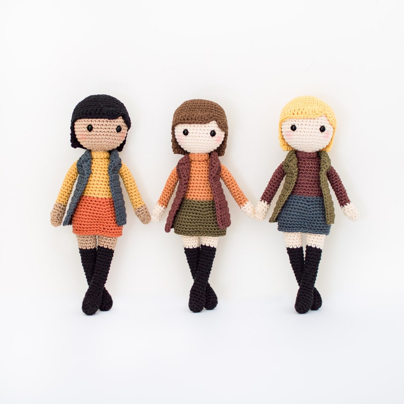 May include: Three crocheted dolls wearing different colored outfits. The dolls have brown hair, black hair, and blonde hair. They are all wearing skirts, vests, and boots.